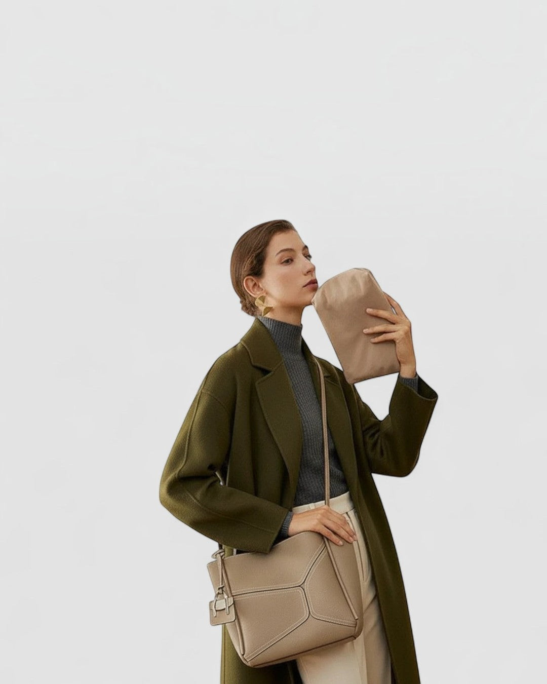 Pine Drew India Becca tote bag in beige vegan leather with gold hardware worn by a model in an olive green coat