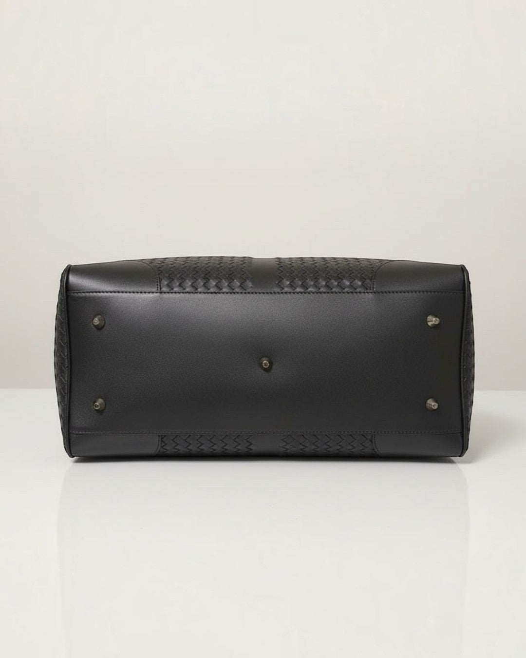 Pine Drew India Monaco woven black leather duffle bag base showing protective metal feet and detailed texture