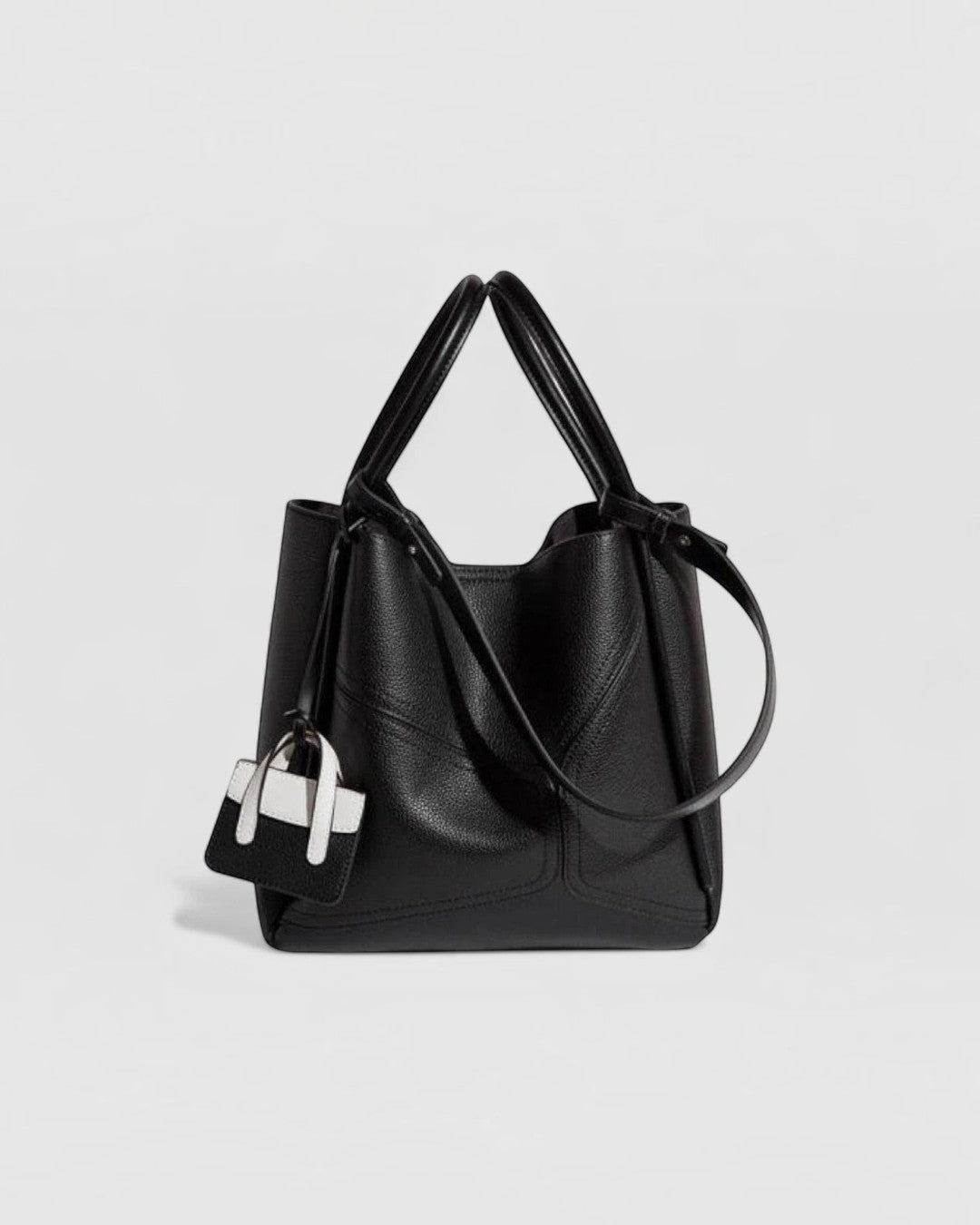 Pine Drew India Becca black vegan leather tote bag with gold hardware, top handles, and a mini bag charm.