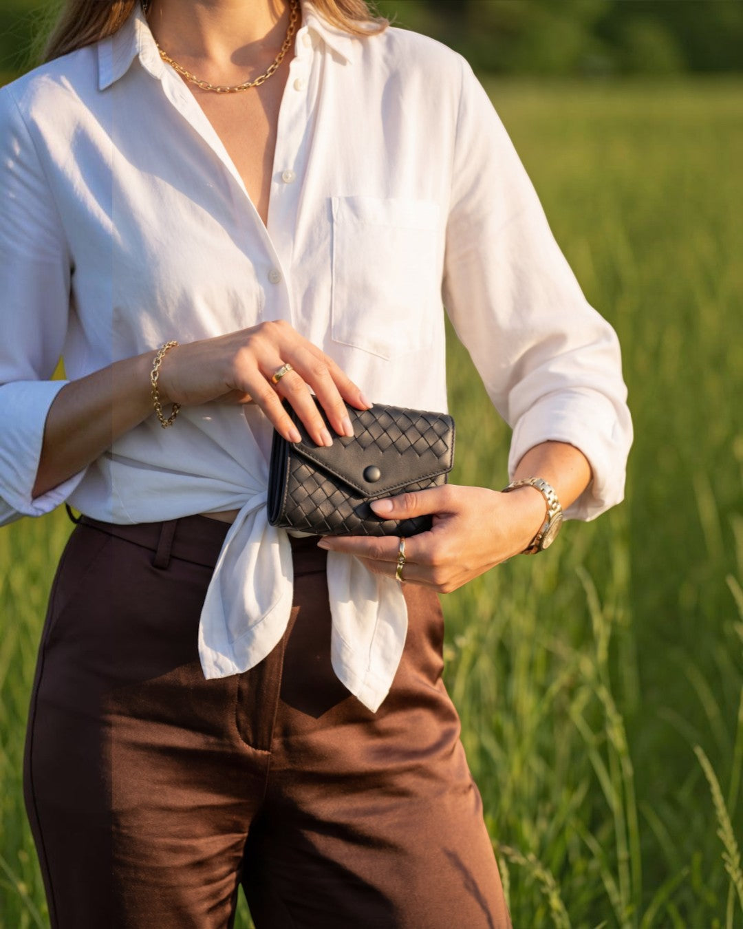 Pine Drew India Caden Interlace black woven leather snap card holder held by a woman in a white shirt in a field.