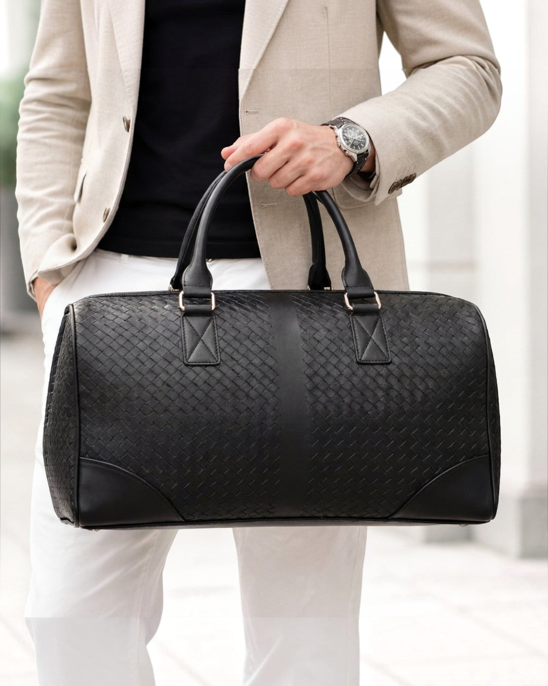 Pine Drew India black woven leather duffle bag held by a man in a beige blazer for travel and business trips