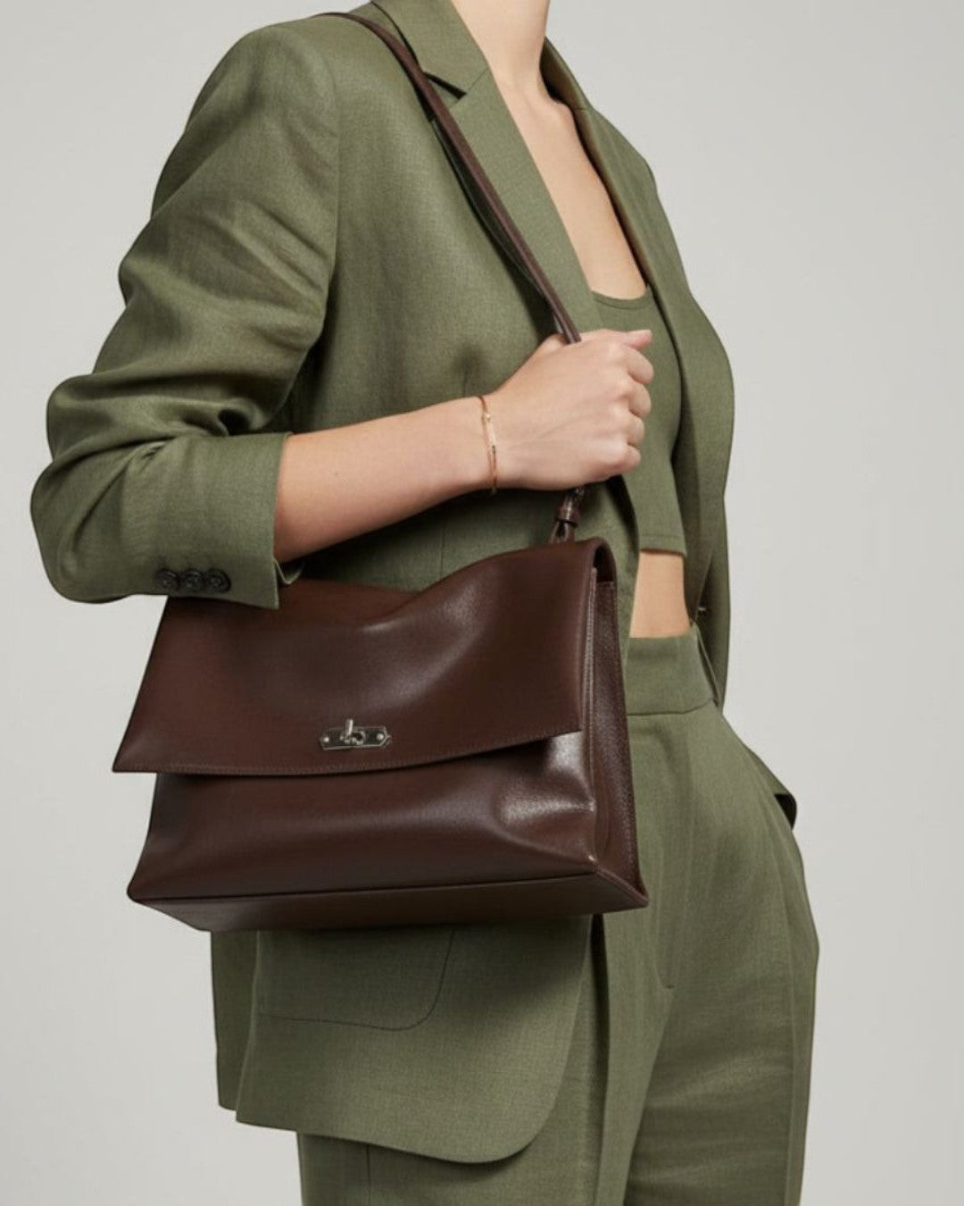 Pine Drew India Cacao Luxe full-grain leather shoulder bag with silver twist-lock hardware on a woman in a green suit