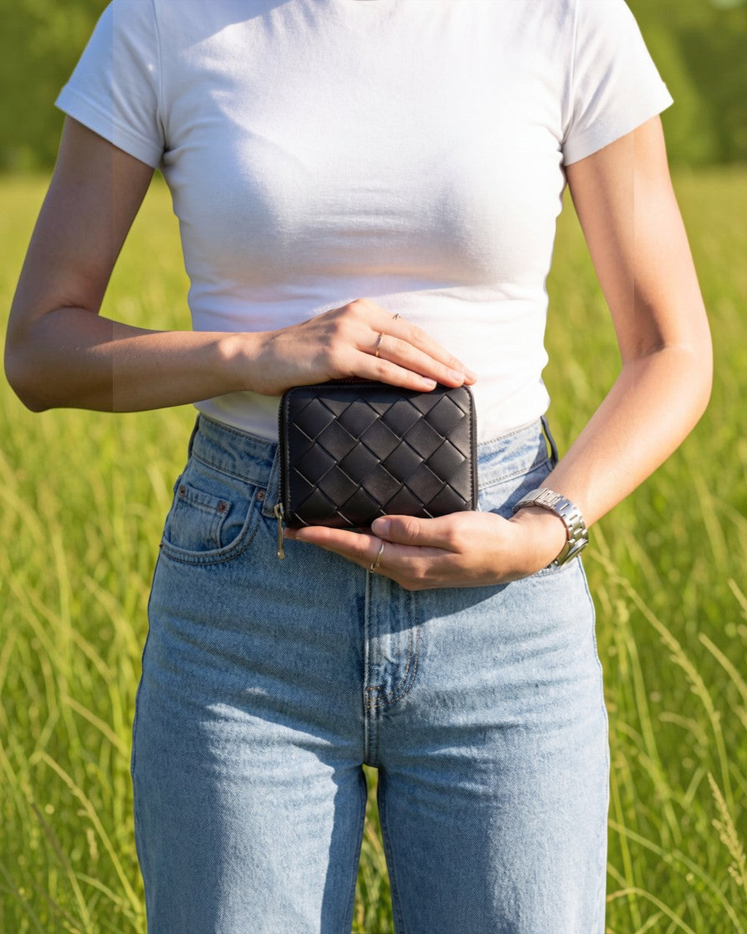 Pine Drew India Caden Interlace zip wallet in black woven leather held by a person in a white t-shirt in a field.