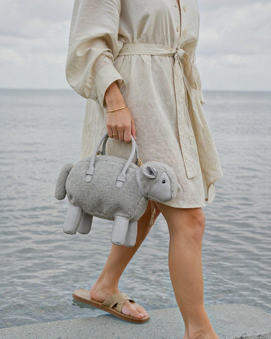Pine Drew India Montone Mini grey sheep-shaped teddy shearling vegan leather bag with structured handles held by a woman