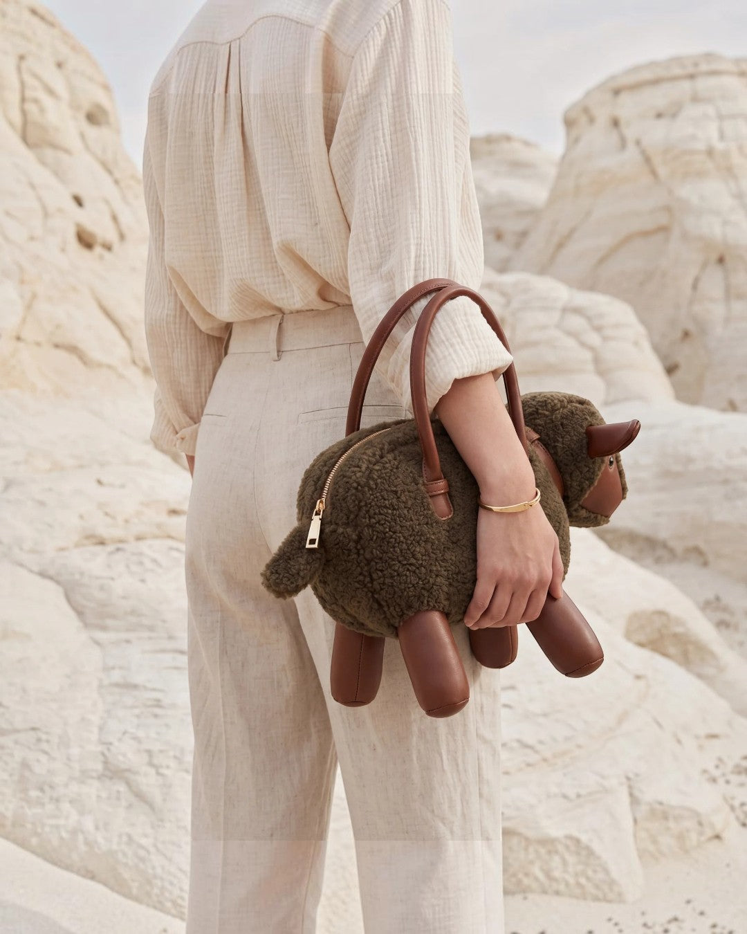 Pine Drew India Montone Mini sheep-shaped bag in chocolate teddy shearling and tan vegan leather held by a woman.