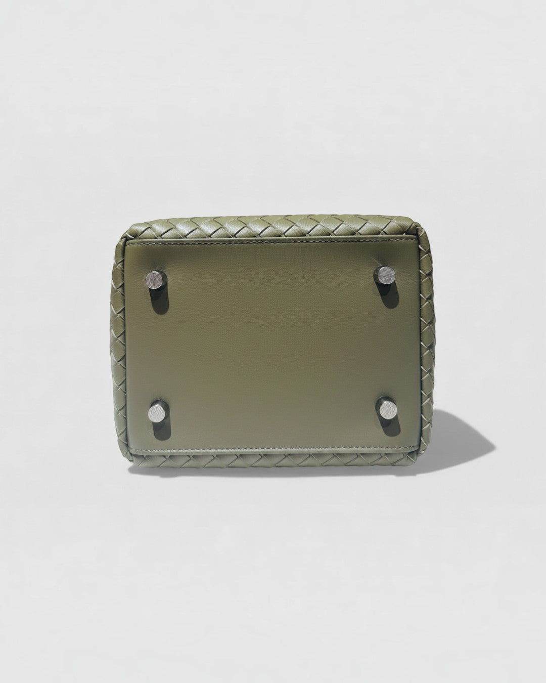 Pine Drew India Luna Verdura olive woven leather handbag base with protective metal feet on a neutral background