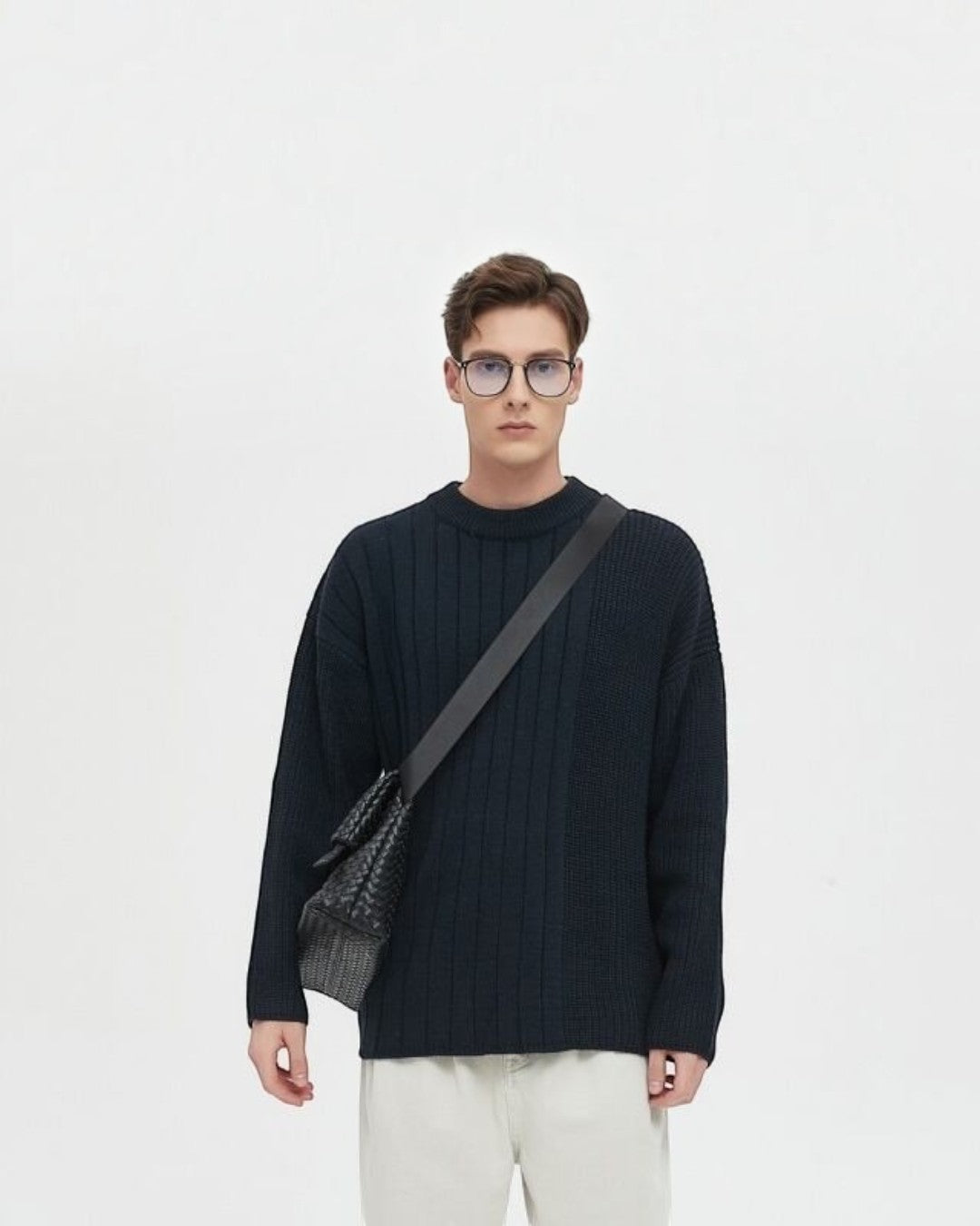 Pine Drew India Ravello foldover weave crossbody bag in black vegan leather worn by a man in a dark ribbed sweater