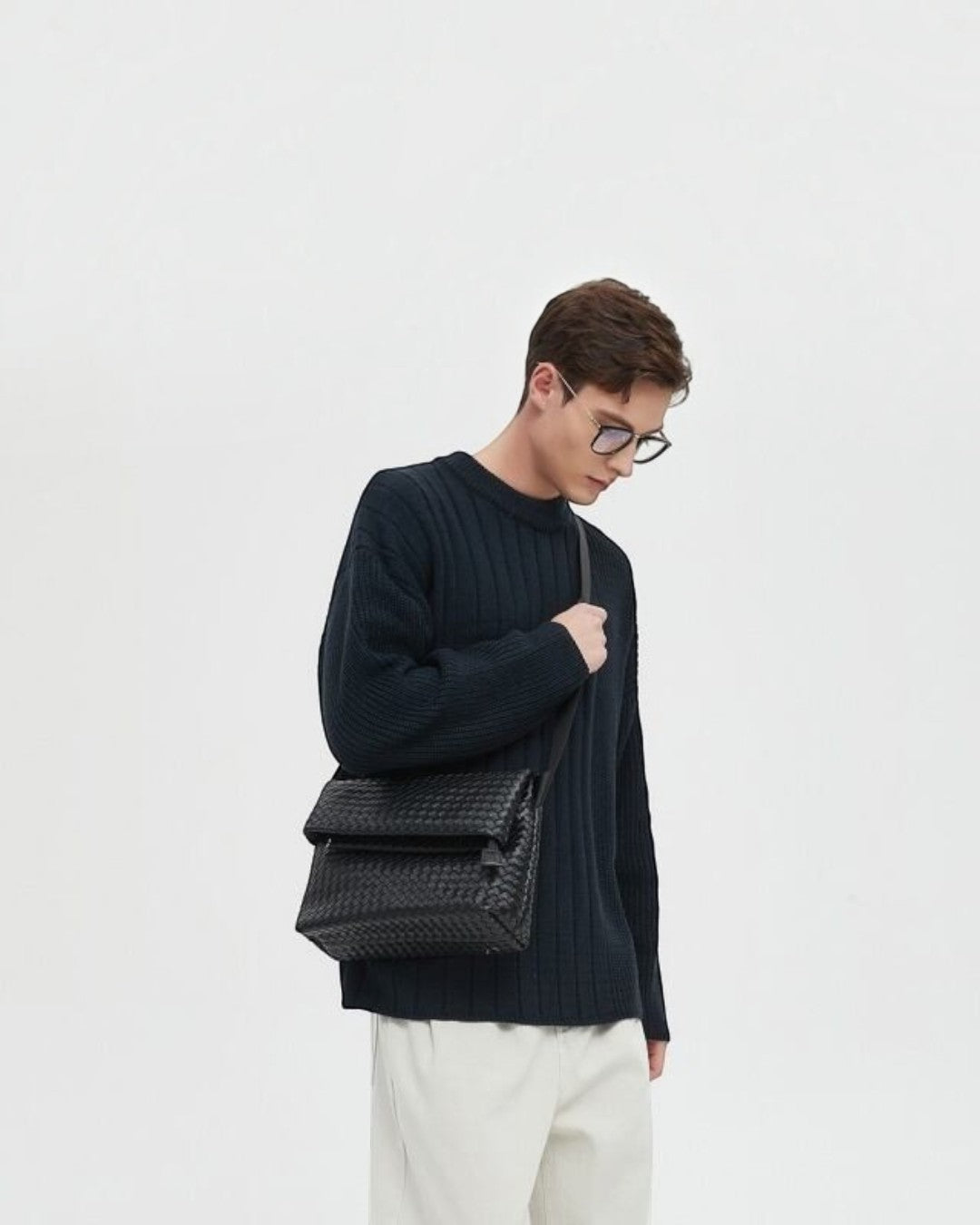 Pine Drew India Ravello black vegan leather crossbody bag with woven texture worn by a man in a dark sweater