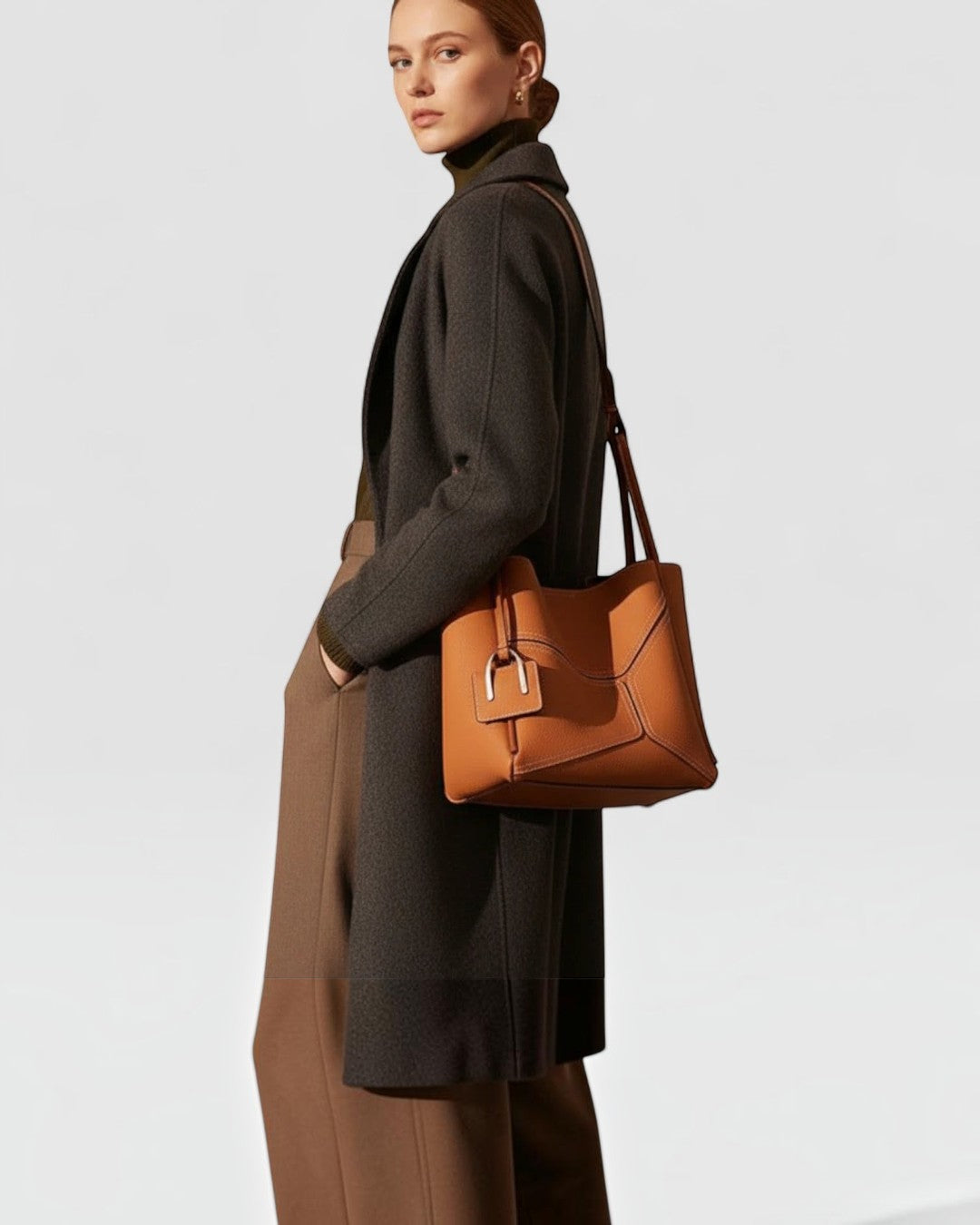 Pine Drew India Becca tote bag in tan vegan leather with gold hardware worn over the shoulder by a model in a coat.