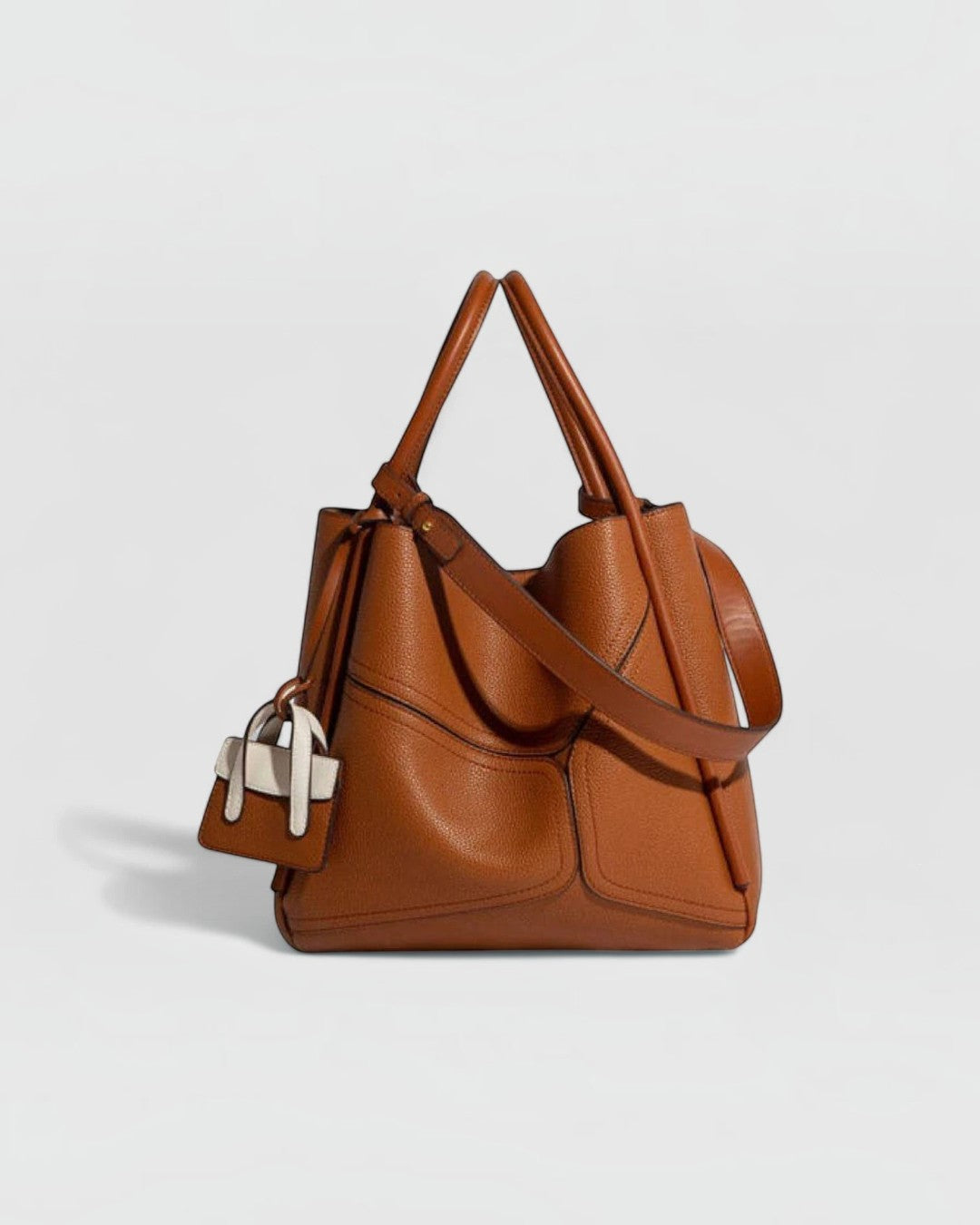 Pine Drew India Becca tote bag in tan vegan leather with gold hardware, adjustable strap, and mini charm accessory.