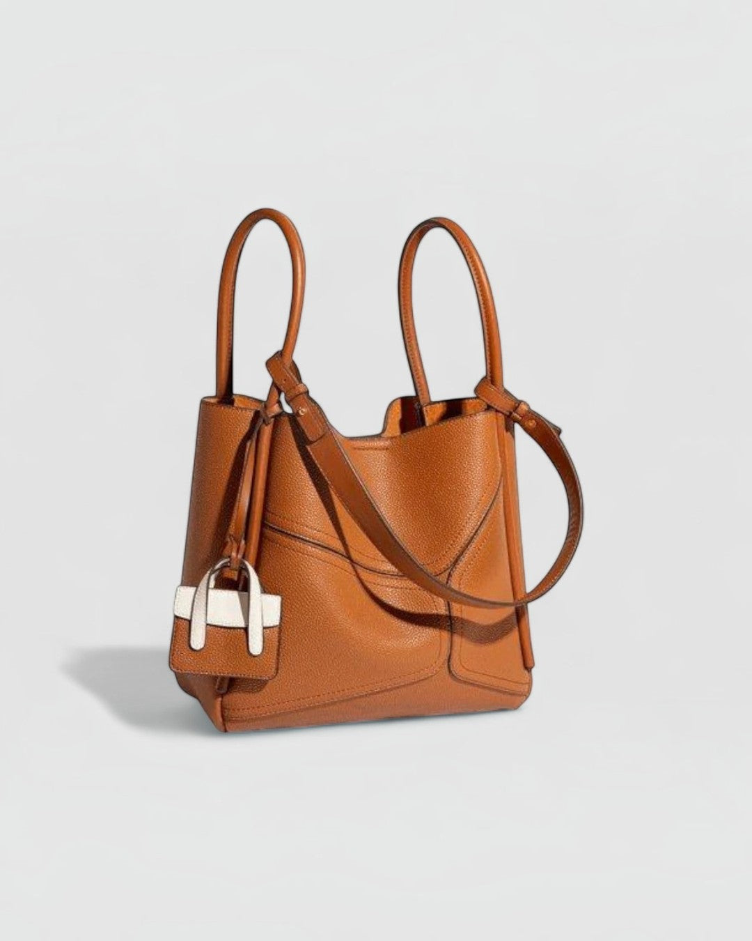 Pine Drew India Becca tote bag in tan vegan leather with gold hardware, dual handles, and a small decorative charm.