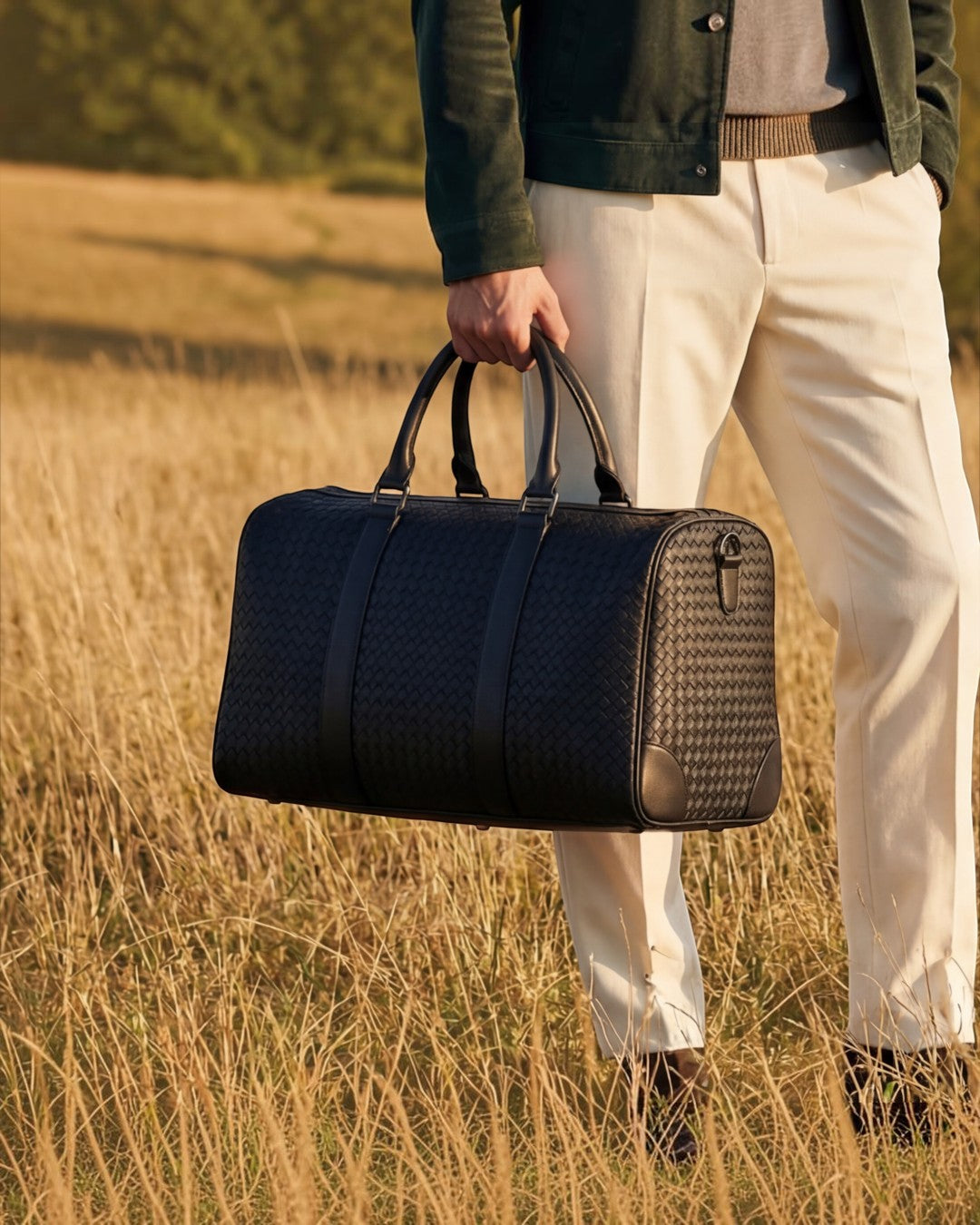 Pine Drew India Elora woven black vegan leather duffle bag held by a man in a field for travel or business.