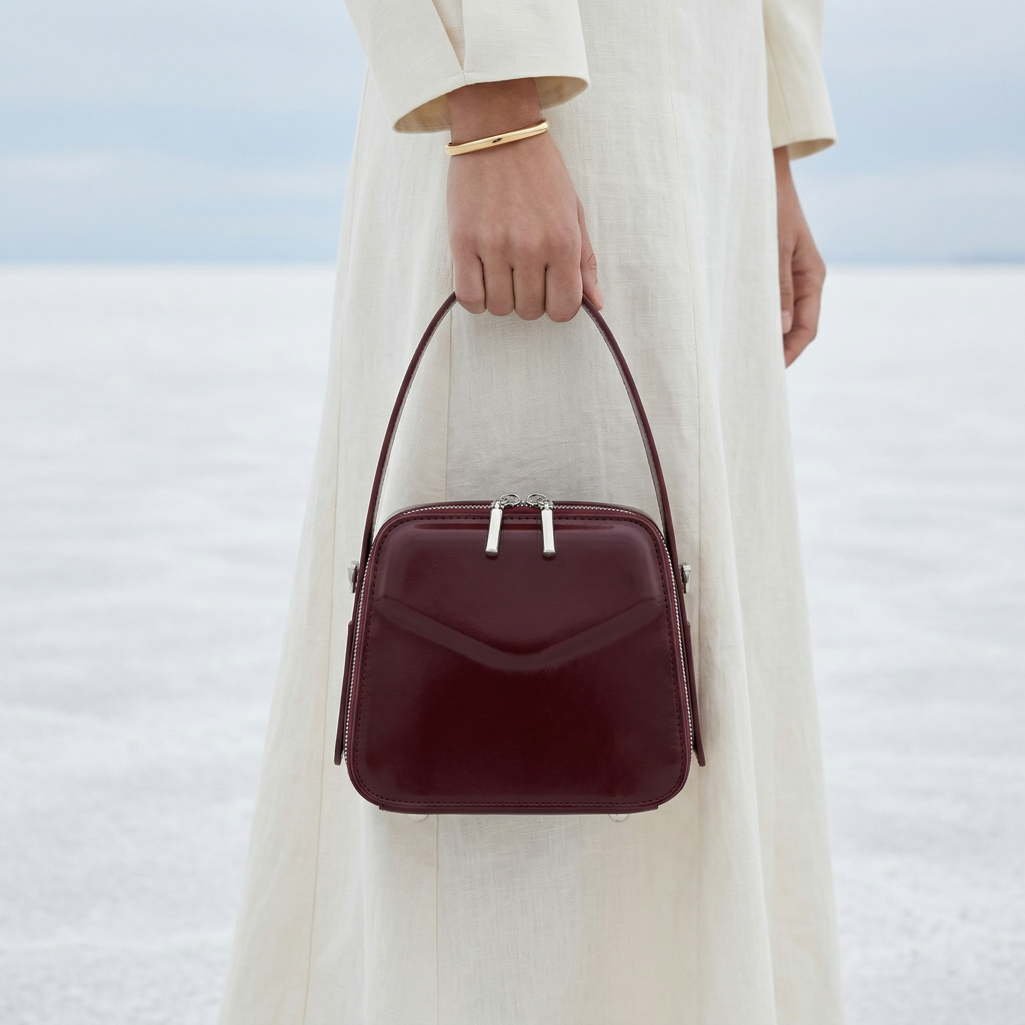 Person holding a burgundy handbag against a blurred natural background