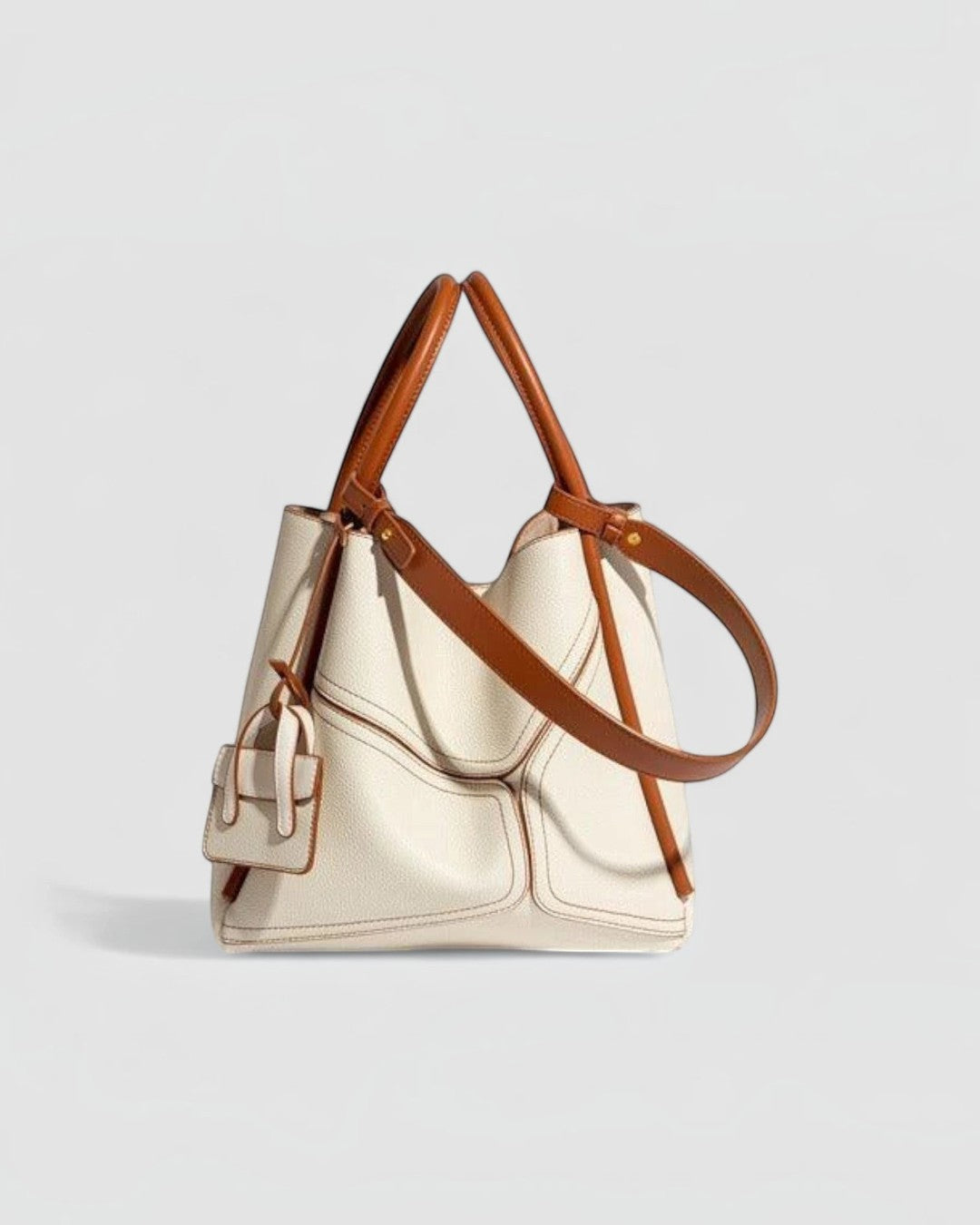 Pine Drew India Becca tote bag in off-white vegan leather with tan trim, gold hardware, and adjustable shoulder strap.