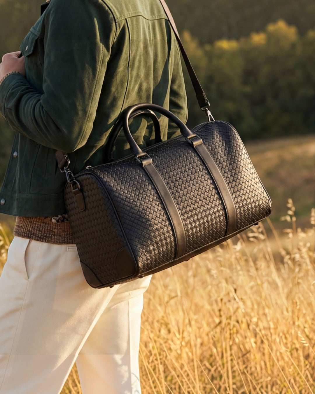 Pine Drew India Elora black vegan leather woven duffle bag carried over the shoulder in a sunny outdoor field.