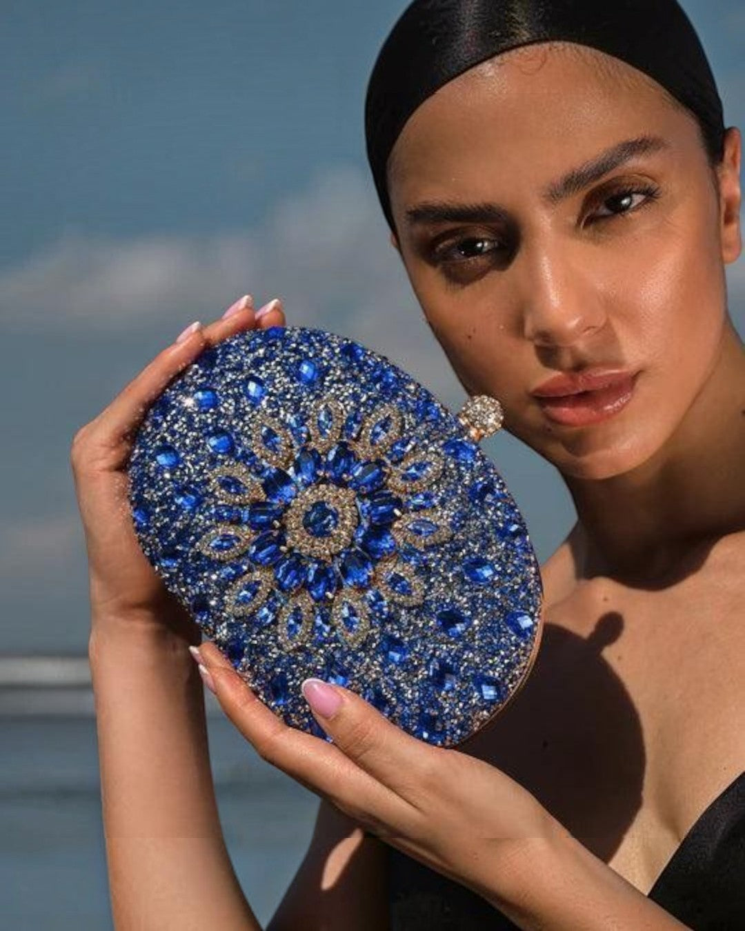 Model holding a Pine Drew India Colette blue diamond-encrusted clutch bag with intricate floral crystal detailing.