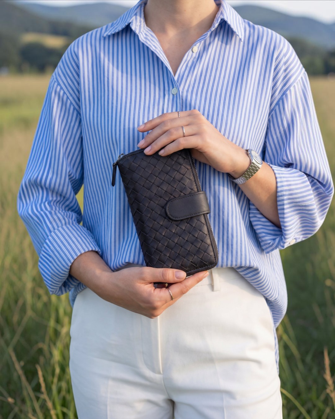 Pine Drew India Caden Interlace long wallet in black woven leather held by a person in a blue striped shirt