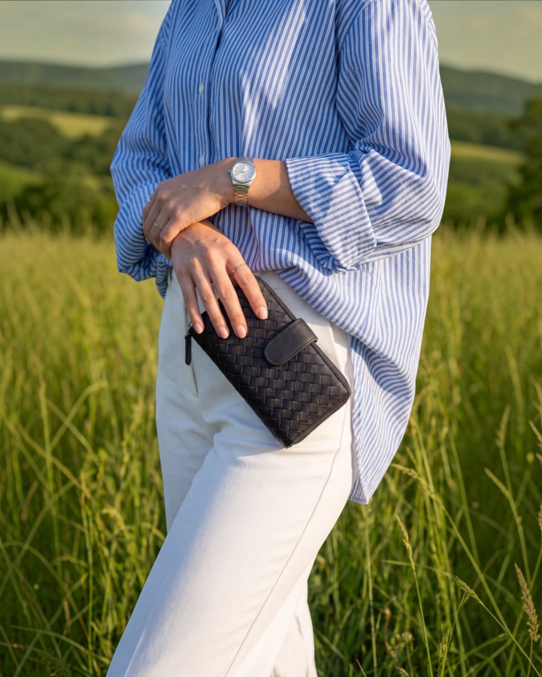 Pine Drew India Caden Interlace long wallet in black woven leather held by a person in a field.