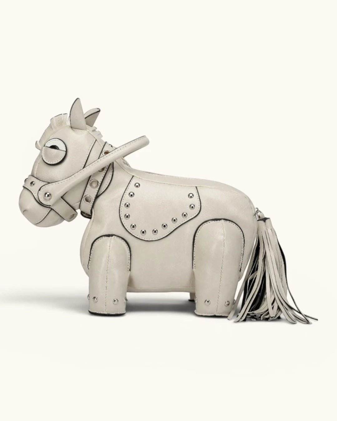 Pine Drew India Cavallo handbag in cream vegan leather shaped like a horse with gold studs and a tassel tail