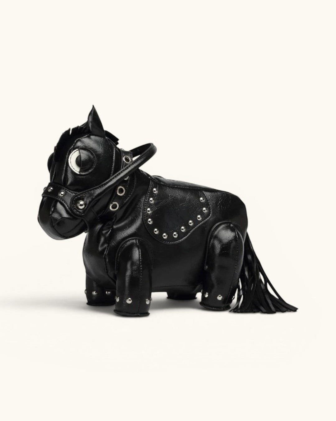 Pine Drew India Cavallo handbag in black vegan leather shaped like a horse with gold stud details and a tassel tail.