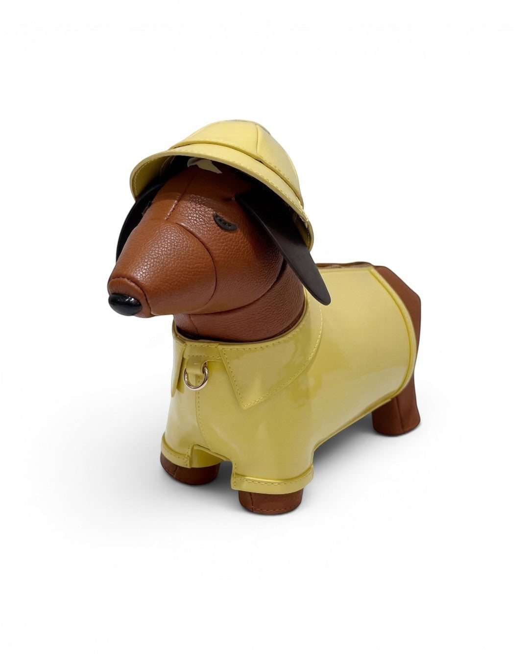 Pine Drew India dachshund-shaped vegan leather bag in brown with a glossy yellow trench coat and safari hat.