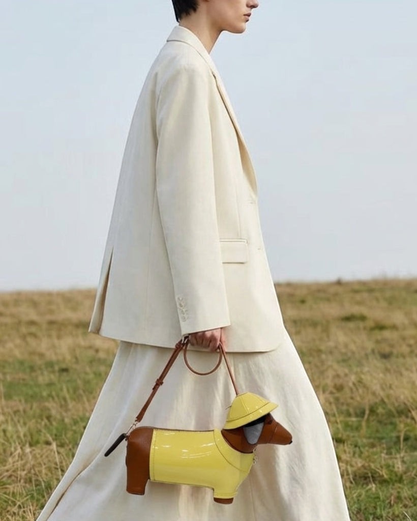 Pine Drew India dachshund shaped vegan leather bag in glossy yellow and brown with gold hardware held by a model