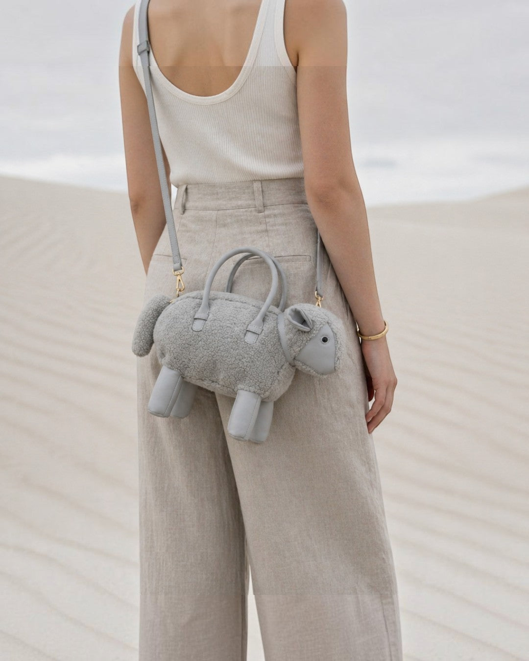 Pine Drew India grey sheep-shaped vegan leather bag with teddy shearling texture worn as a crossbody in a desert.