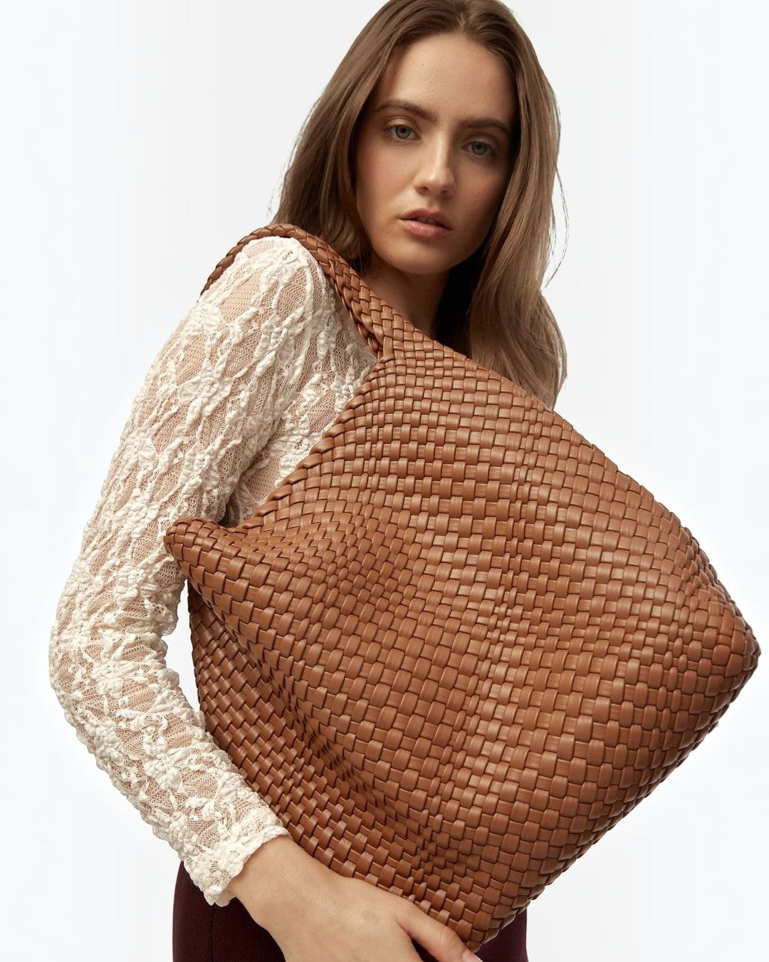 Pine Drew India Jocelyn handwoven brown vegan leather shoulder bag carried by a woman in a white lace top