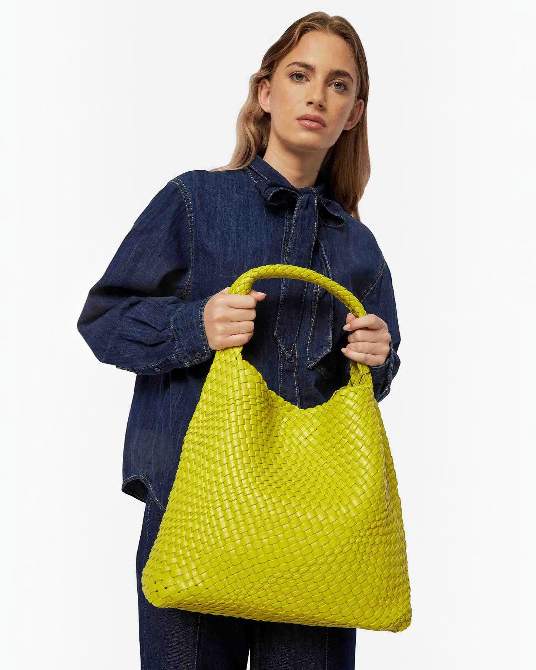 Pine Drew India Jocelyn bag in bright lime green handwoven vegan leather held by a woman in a denim shirt