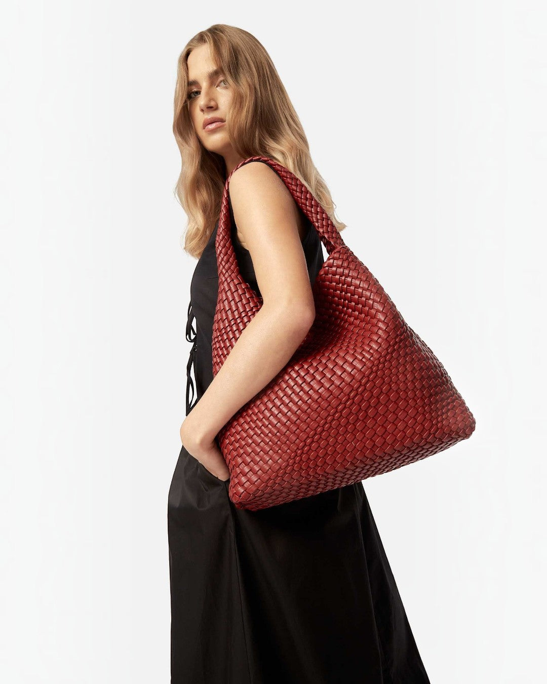Pine Drew India Jocelyn bag in deep red handwoven vegan leather worn over the shoulder by a woman in a black dress