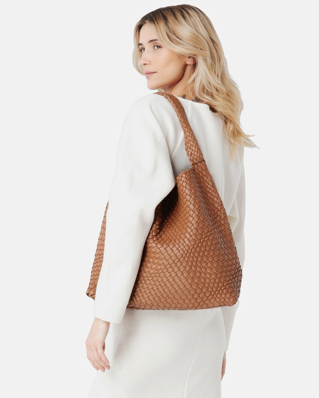 Pine Drew India Jocelyn bag in tan handwoven vegan leather worn over the shoulder by a blonde woman in a white coat