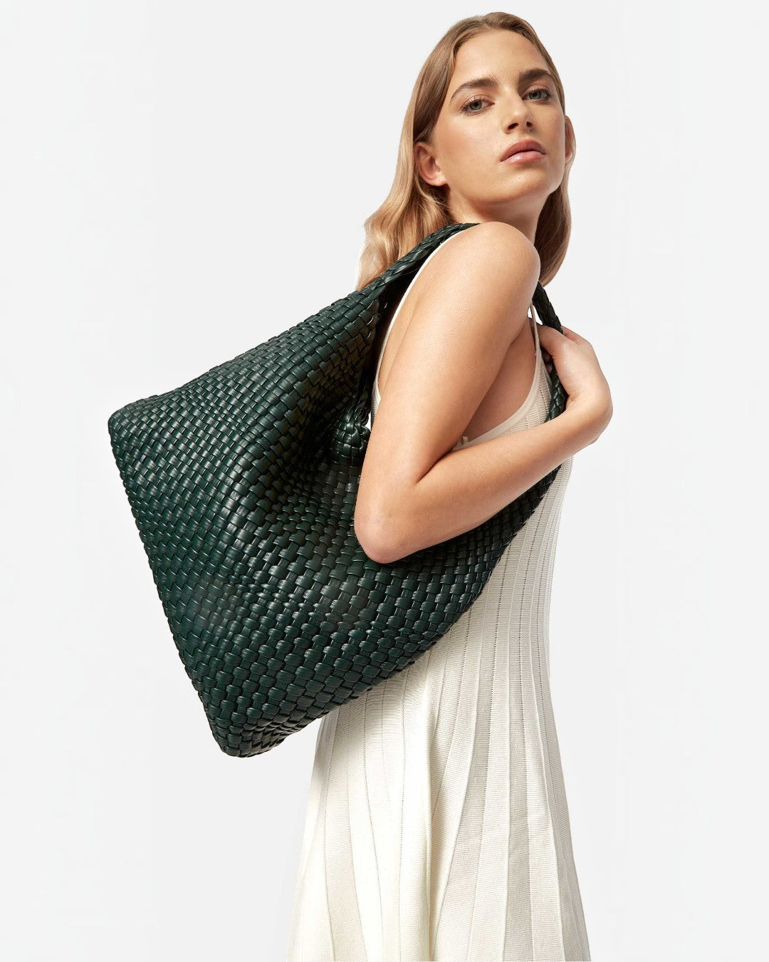 Pine Drew India Jocelyn handwoven dark green vegan leather shoulder bag worn by a woman in a white dress