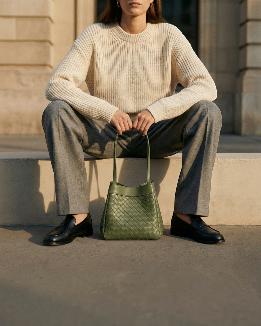 Pine Drew India Luna Verdura olive green woven leather handbag with architectural handles held by a seated model.