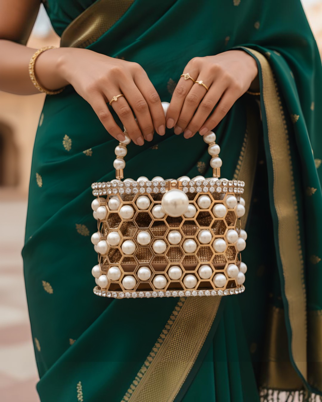 Pine Drew India champagne-gold honeycomb lattice minaudière bag adorned with pearls, held by a woman in a green sari.