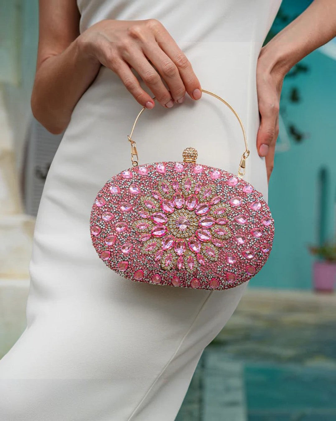 Pine Drew India pink diamond encrusted oval clutch bag with gold handle held by a woman in a white dress
