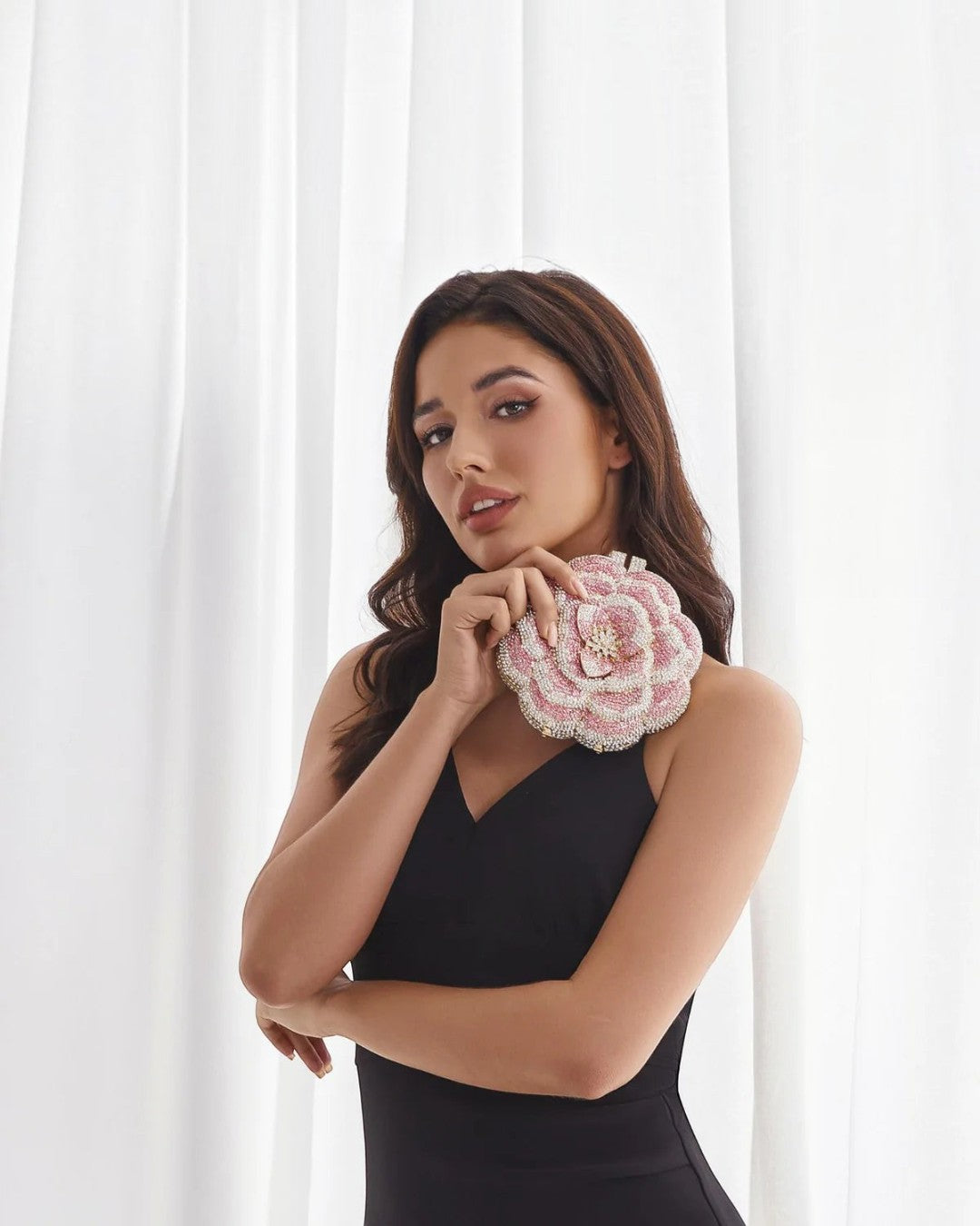 Pine Drew India pink floral clutch bag with rhinestone embellishments held by a woman in a black dress.