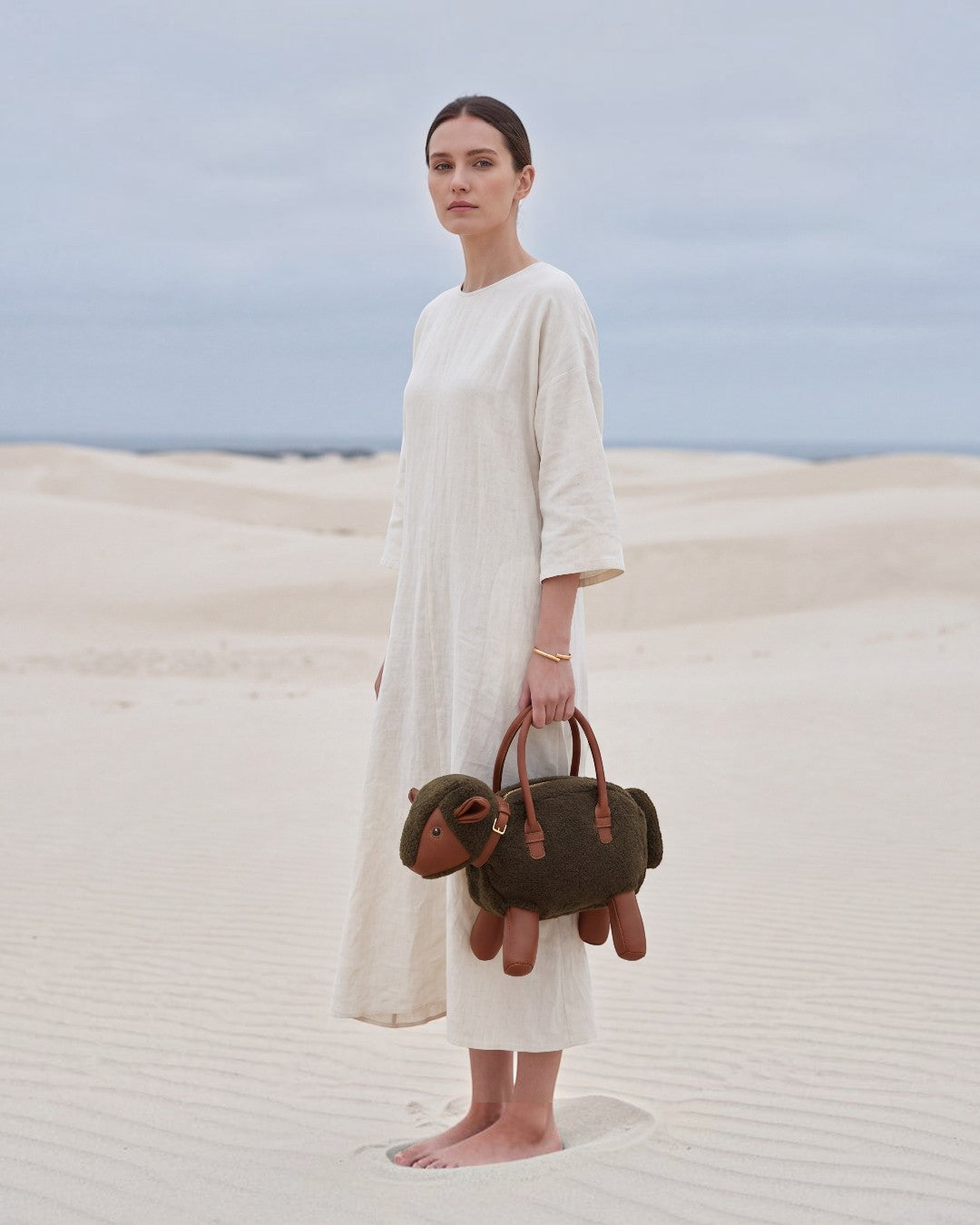 Pine Drew India Montone Mini sheep-shaped bag in chocolate teddy shearling and tan vegan leather held by a model.