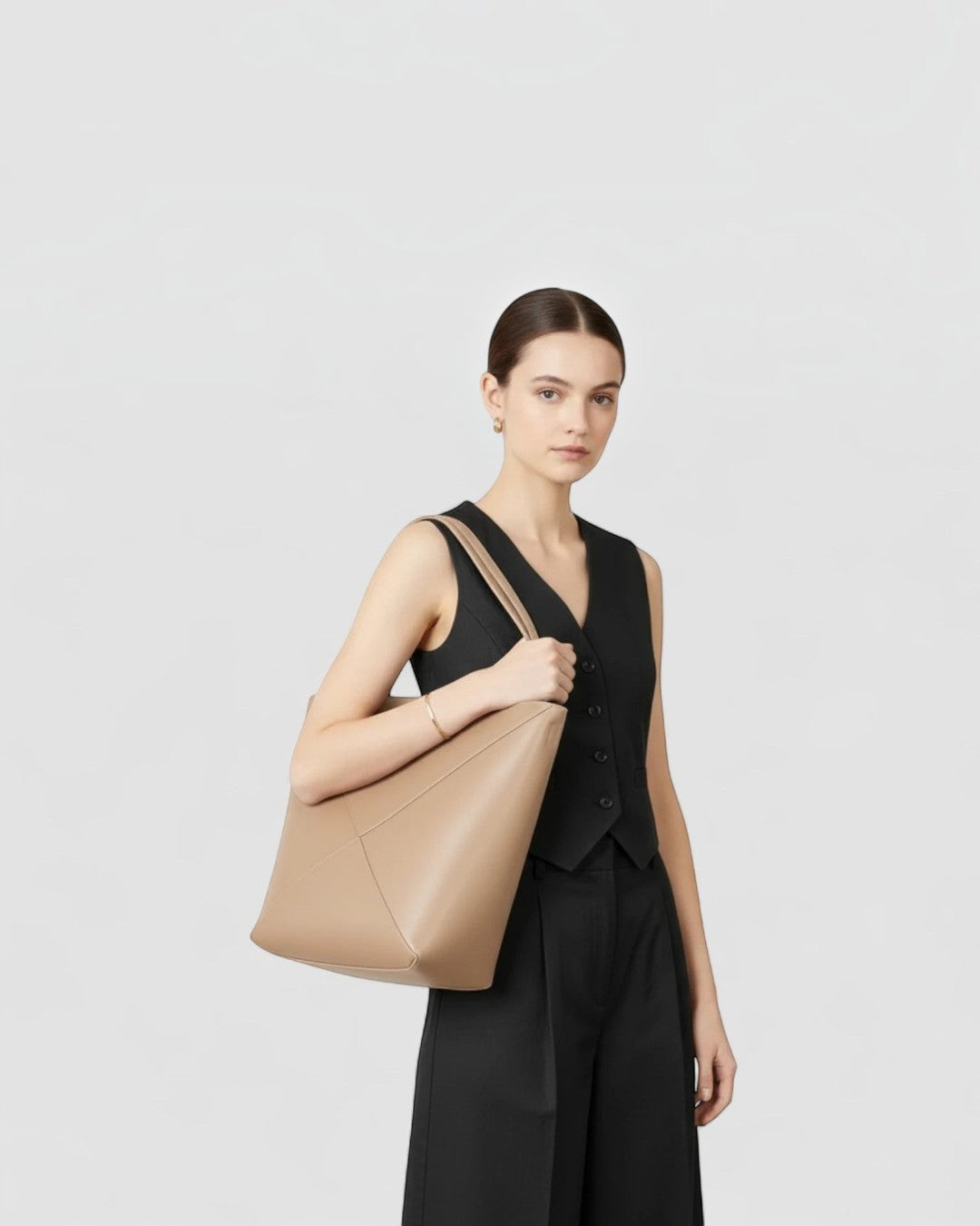 Model wearing a Pine Drew India tan full-grain leather EDA tote bag with geometric panels and a vertical silhouette.