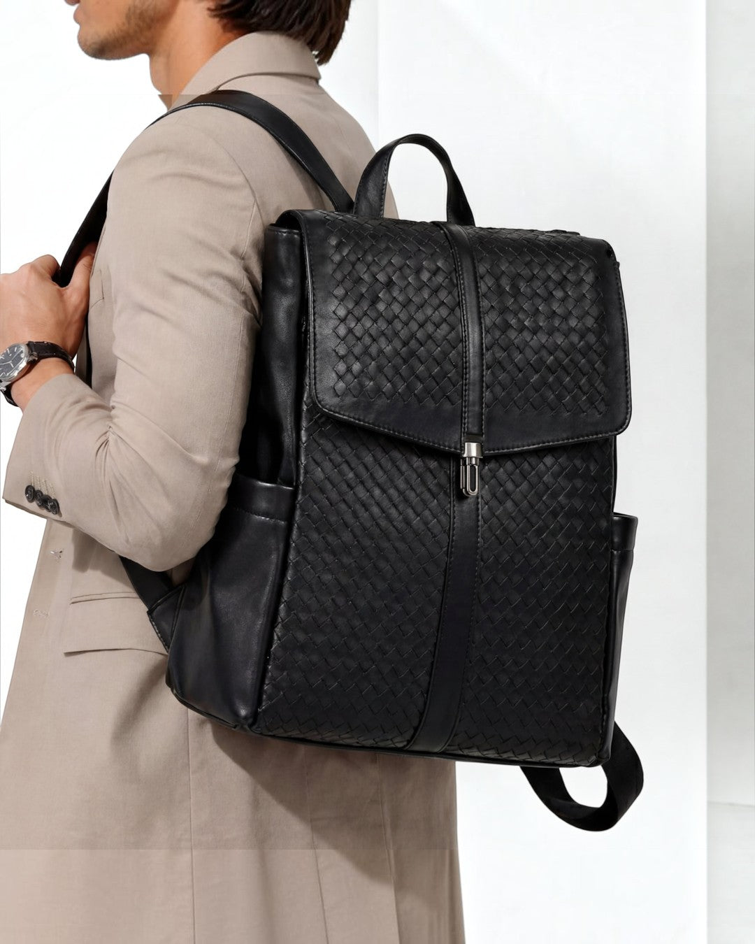 Pine Drew India Torrenzo black vegan leather backpack with woven front panel and flap closure worn by a man in a suit.