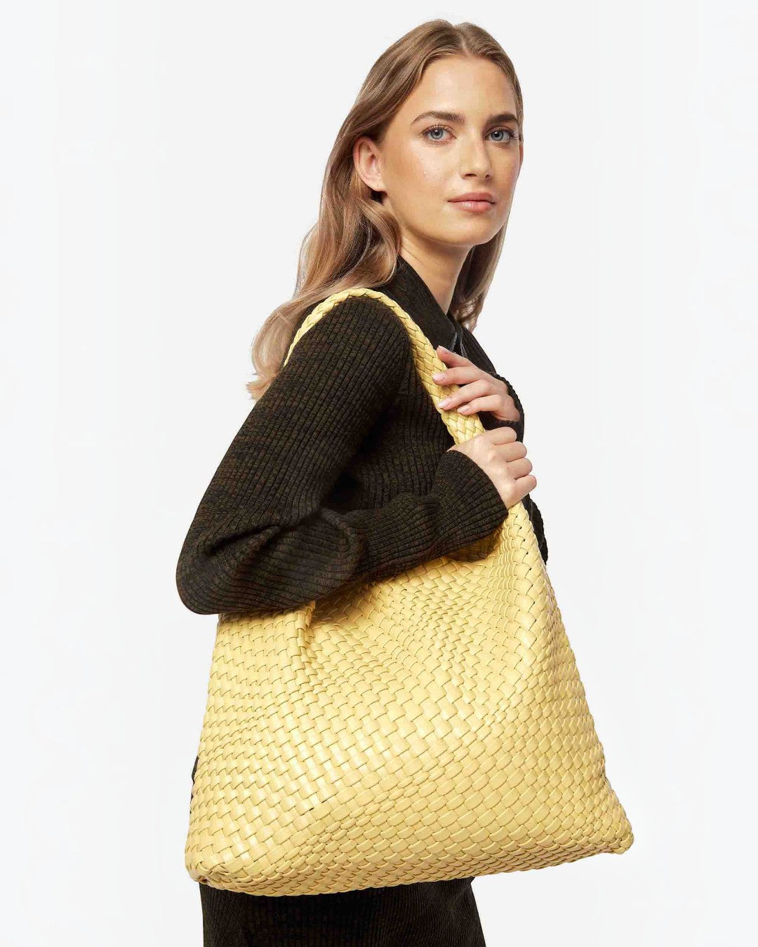 Model carrying a yellow handwoven vegan leather shoulder bag by Pine Drew India with a slouchy sculptural design.